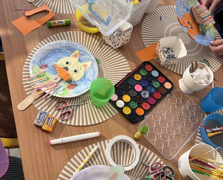 Tisch mit bunter Bastelmaterialien, bemalten Tellern und kreativen Kunstwerken.