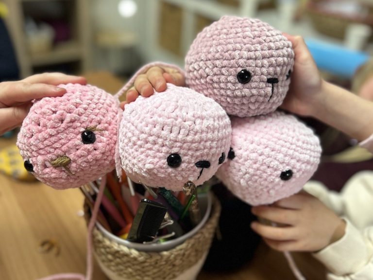 Teilnehmerinnen häkeln gemeinsam an einem Tisch mit bunten Wollknäueln in der Kreativwerkstatt.
